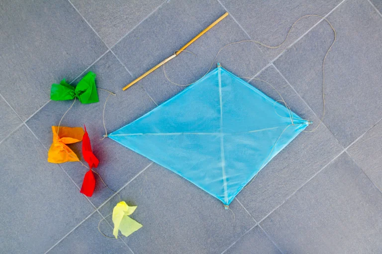 Blauer Rautendrachen aus Transparentpapier mit Holzstab, Drachenschnur und buntem Krepp-Schwanz – Drachen basteln mit Kindern.