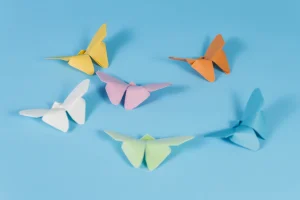Sechs farbige Origami Schmetterlinge aus Papier auf blauem Hintergrund, in lockerer Kreisform angeordnet.