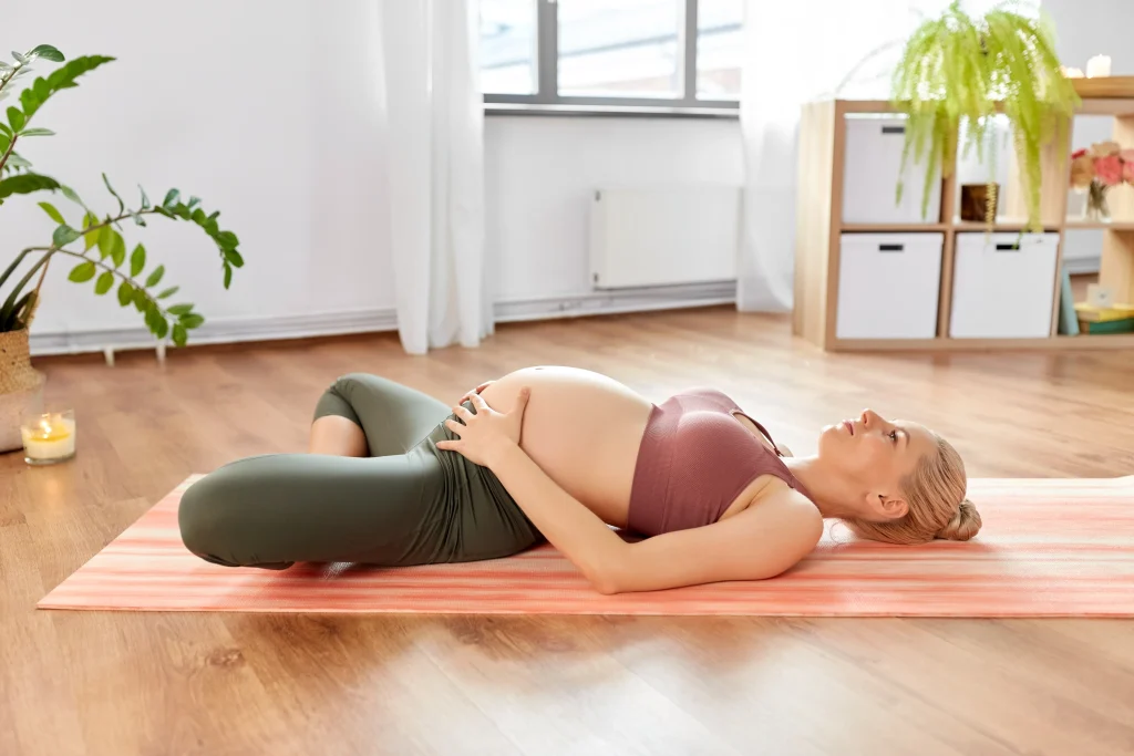 Schwangerschaftsyoga: Schwangere Frau liegt im unterstützten Schmetterling (Supta Baddha Konasana) auf der Matte und hält die Hände am Bauch.