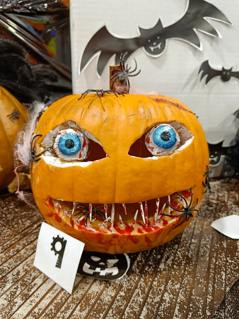 Halloween Deko basteln mit Kindern – geschnitzter Kürbis mit Papierzähnen, Schoko-Augen und Plastikspinnen als gruselige Deko