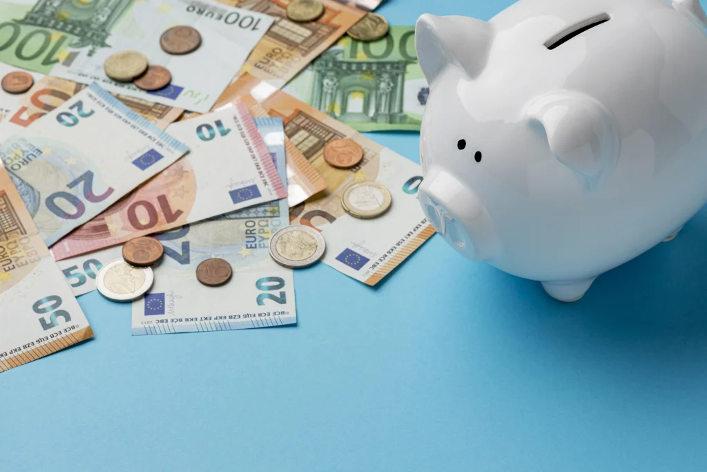 Weißes Sparschwein neben verteilten Euro-Scheinen und Münzen auf blauem Hintergrund – Symbolbild für Kindergeld 2026 und Familienbudget.