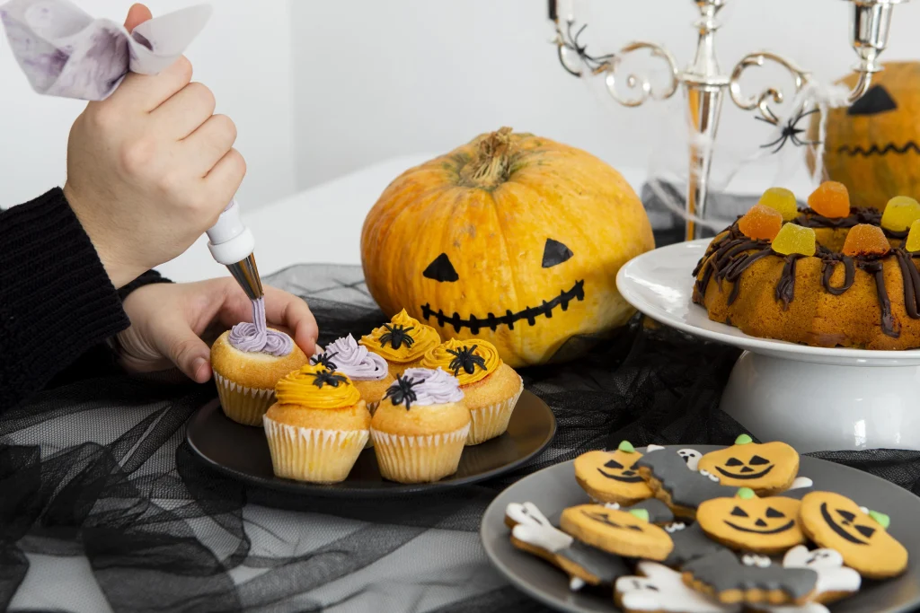 Halloween Deko basteln mit Kindern – Cupcakes mit lila und orangener Creme, Spinnen-Deko, Kürbis-Kuchen und Plätzchen auf einem Halloween-Buffet