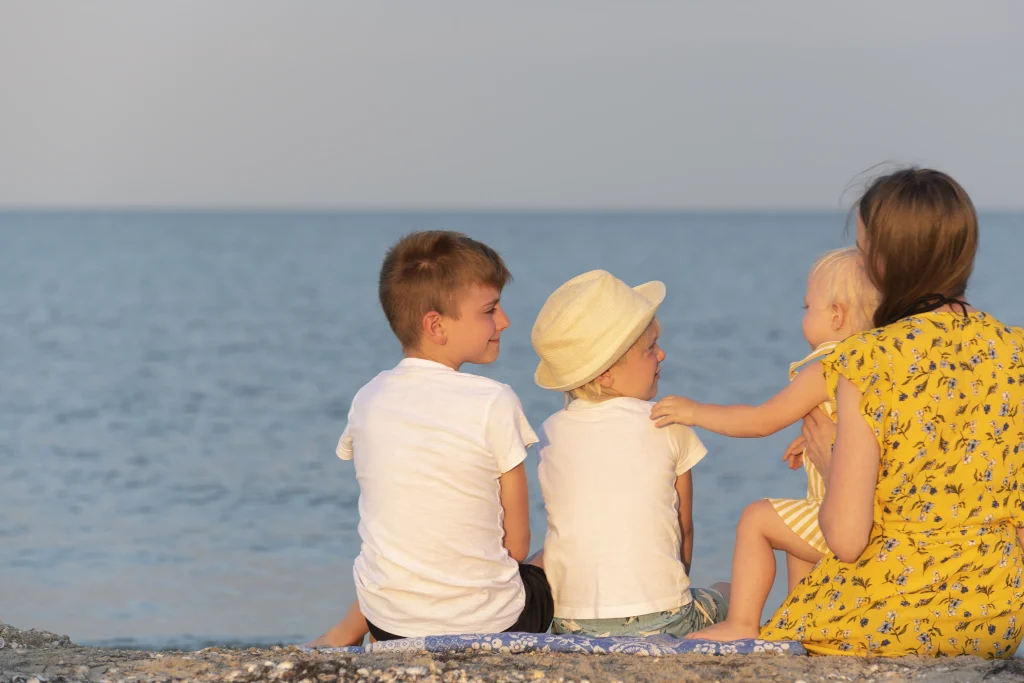 Mutter mit drei Kindern am Strand schaut aufs Meer – harmonische Familienzeit, perfekt zur Planung von Kita-Schließtagen und Schulferien 2026