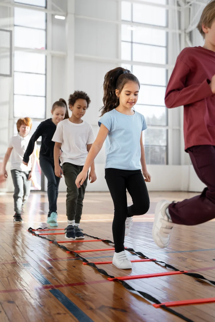 Kinderturnen in der Turnhalle – Gruppe von Kindern läuft nacheinander über eine Koordinationsleiter; Übung für Schnelligkeit, Fußkoordination und Rhythmus