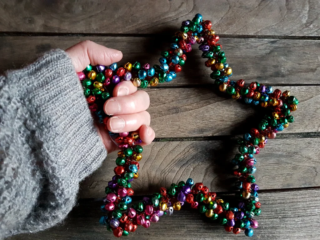 Hand hält einen bunten Stern aus kleinen Glöckchen – kreative Weihnachtsdeko zum Basteln mit Kindern.