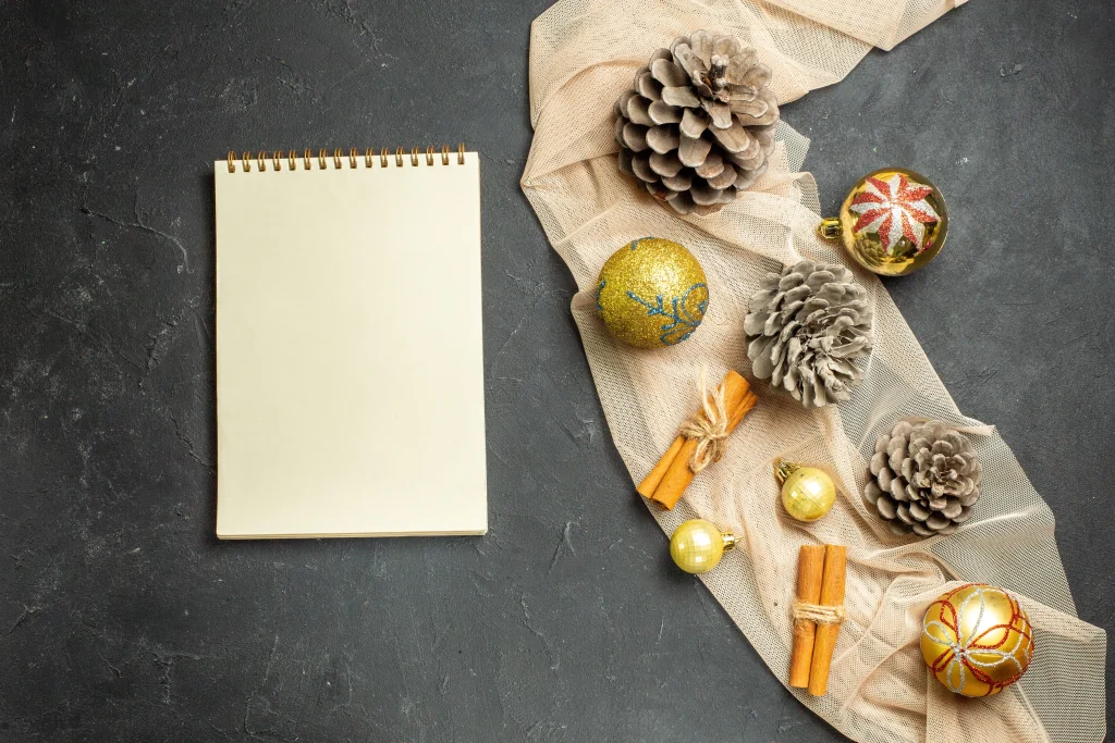 Weihnachtliche Materialien wie Zapfen, Zimtstangen und Kugeln liegen neben einem leeren Notizblock – Vorbereitung für Bastelideen mit Kindern.