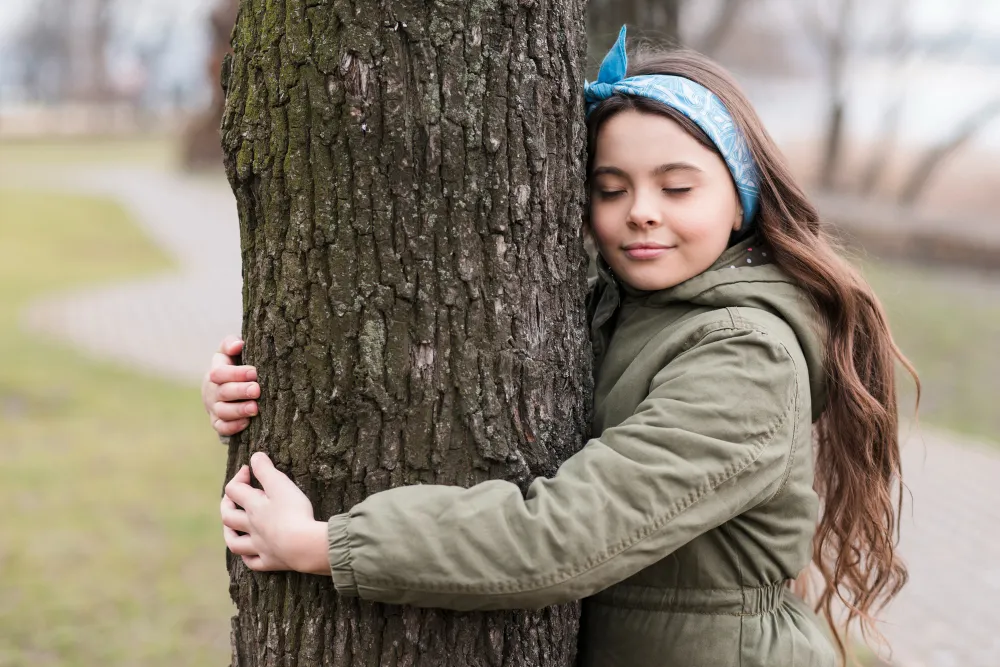 Mädchen umarmt einen Baum in der Natur – Symbol für emotionale Stärke und Resilienz bei Kindern
