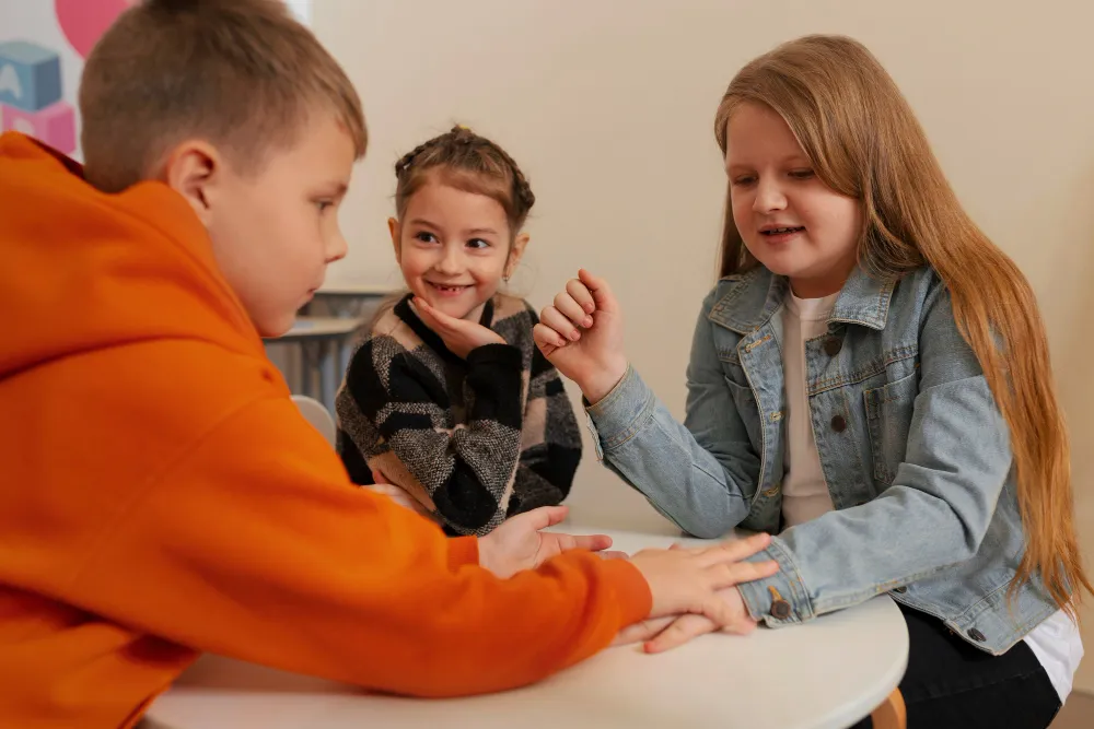 Kinder spielen gemeinsam ein Fingerspiel am Tisch – soziale Interaktion stärkt Resilienz bei Kindern