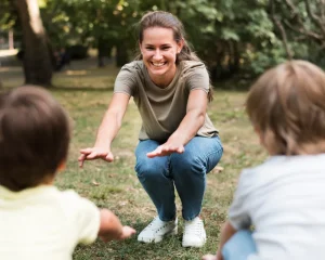 Selbstständige Erzieherin leitet einen Naturpädagogik-Kurs im Freien und interagiert spielerisch mit zwei Kindern auf Augenhöhe.