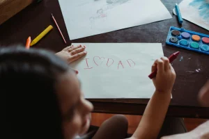 Kind bastelt ein Vatertagsgeschenk und malt „I love Dad“ auf Papier