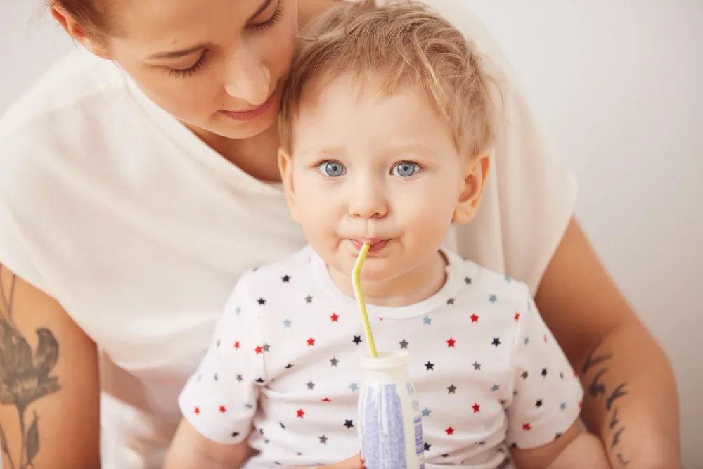 Baby trinkt Kuhmilch aus einer Flasche mit Strohhalm auf dem Schoß der Mutter