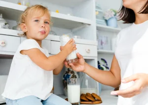 Kleinkind trinkt ein Glas Kuhmilch mit Unterstützung der Mutter in der Küche
