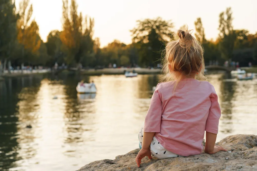Mädchen sitzt am Ufer eines Sees und blickt auf das Wasser – Familienausflug an einem der schönsten Seen Deutschlands.