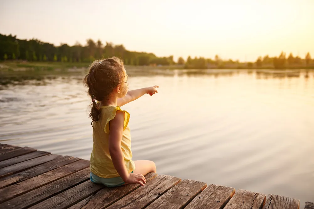 Kleines Mädchen sitzt auf einem Holzsteg an einem See und blickt über das Wasser – Familienausflug an einem der schönsten Seen Deutschlands.