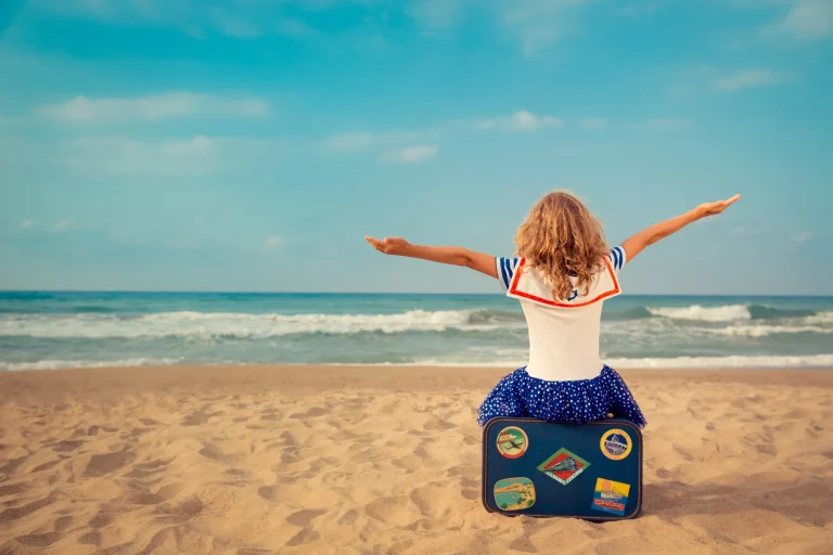 Kind mit Reisekoffer am Strand als Symbol für Schulferien 2027 und Familienurlaub