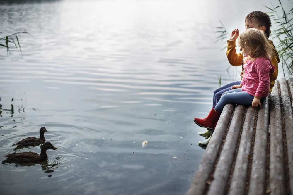 Zwei Kinder sitzen am Ufer eines Sees und beobachten Enten – Familienausflug an einem der schönsten Seen Deutschlands.