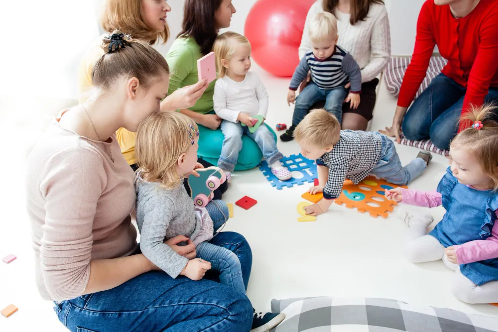 Eltern betreuen und begleiten Kleinkinder beim gemeinsamen Spielen in einem hellen Kita-Raum.
